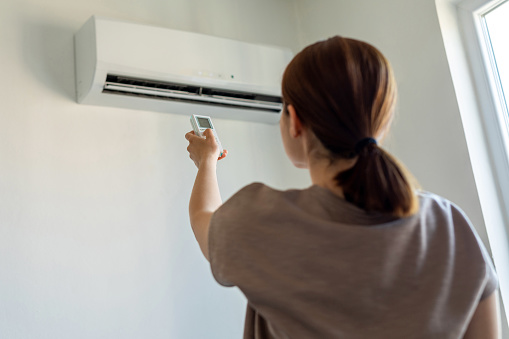 Woman turning on air conditioner with remote