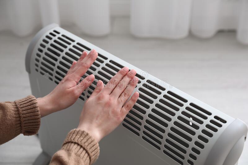 woman-warm-hands-near-electric-heater-home-closeup-211095009